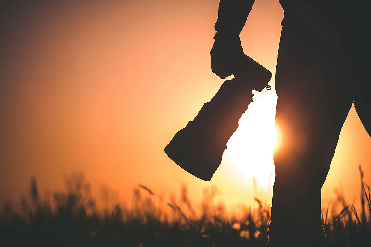 a person's hand holding a camera in front of a sunset